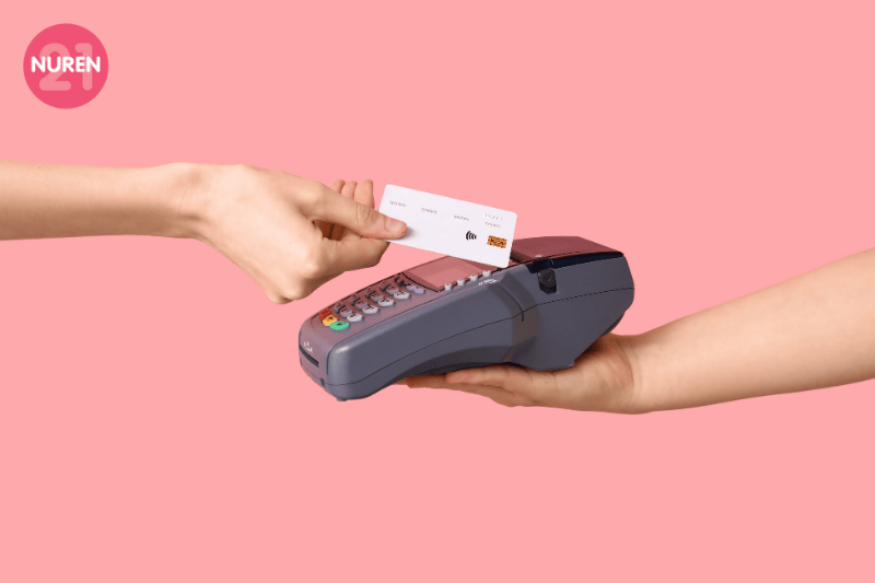 image of one hand tapping the card of a credit card machine with pay wave on an isolated pink background