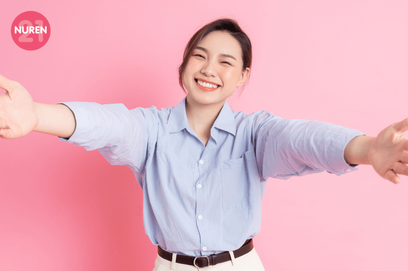 girl in light blue casual oxford shirt offering a hug pictured in a pink background