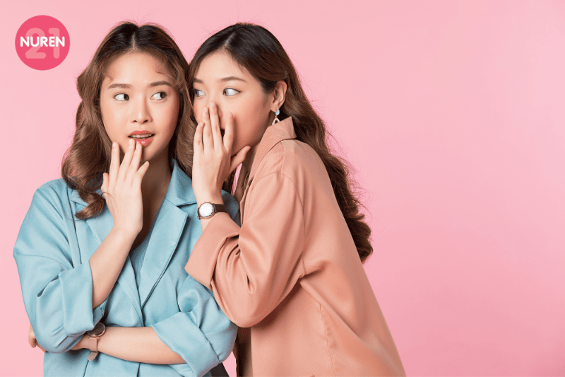 2 girls sharing secret with each other during photoshoot in front of pink screen