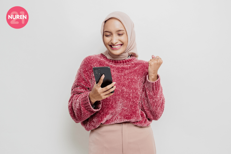 woman in pink sweater with hijab looking excited with phone