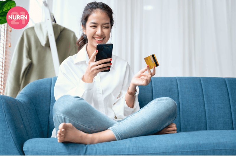 girl holdng credit card ready to do some online shopping while looking into phone sitting on a blue sofa