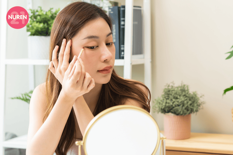 image of girl putting on light eyeliner while looking at portable mirror and sitting on a dressing table