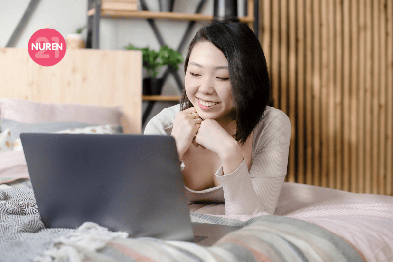 woman in home clothes of pastel colors in the bedroom on the bed uses a laptop
