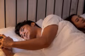 Asian man secretly chatting to mistress while lying in bed with girlfriend. Attractive disloyal husband using phone communicate with paramour lover while his wife sleeping late at night in bedroom.