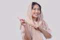 Happy young Asian Muslim woman wearing hijab pointing to the copy space behind her
