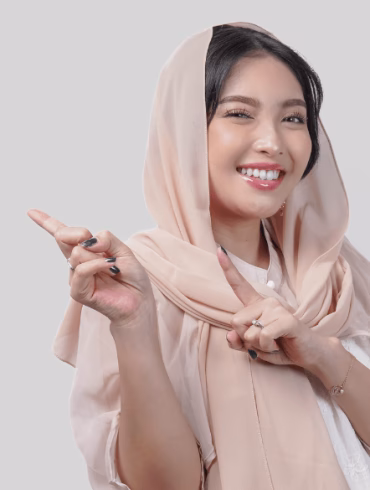 Happy young Asian Muslim woman wearing hijab pointing to the copy space behind her