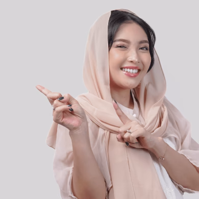 Happy young Asian Muslim woman wearing hijab pointing to the copy space behind her