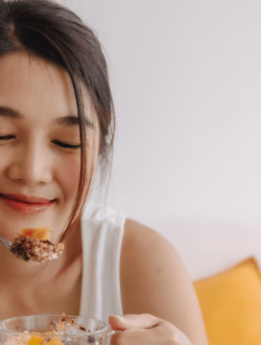 girl holding a yogurt bowl and enjoying some toppings like nuts and fruits