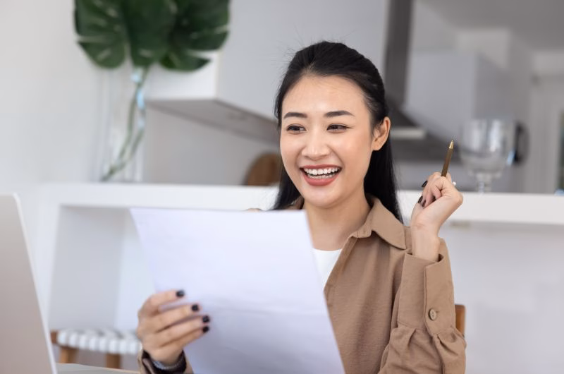 Asian woman reading letter or document with happy personal news,