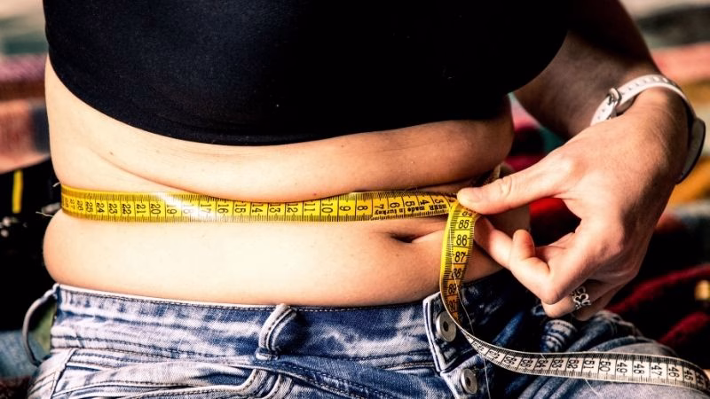woman overweight using measuring tape to check waist size