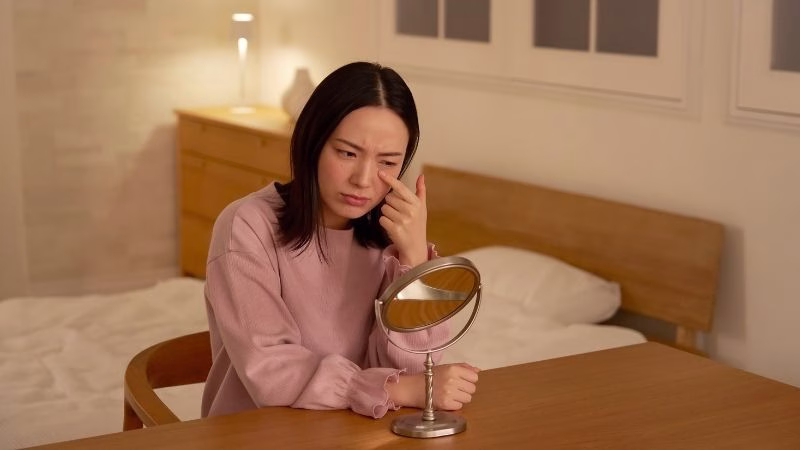 woman looking at her face in the mirror and feeling worried