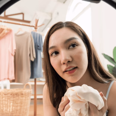 Young Asian woman holds white knitwear near washing machine door, friendly home lifestyle laundry preparation, tidy apartment clothing care, weekend domestic chore and organized wardrobe routine