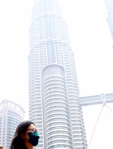 People wearing face mask walking infront of Kuala Lumpur Twin Tower surrounding by haze.