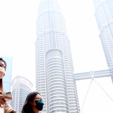 People wearing face mask walking infront of Kuala Lumpur Twin Tower surrounding by haze.