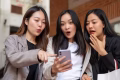 Excited and amazed young Asian women are looking at a smartphone screen with shocked faces, surprising with an online hot deal, and enjoying shopping day in the city together. Shopping and fashion