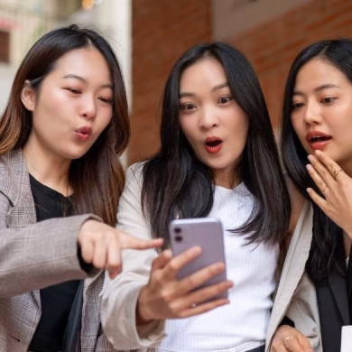 Excited and amazed young Asian women are looking at a smartphone screen with shocked faces, surprising with an online hot deal, and enjoying shopping day in the city together. Shopping and fashion