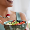 Close up of athletic woman eating a healthy fruit bowl in the kitchen at home