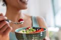 Close up of athletic woman eating a healthy fruit bowl in the kitchen at home
