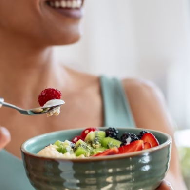 Close up of athletic woman eating a healthy fruit bowl in the kitchen at home