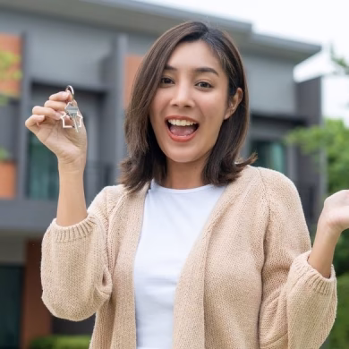 Woman buying or rent new home she holding key front of new house. Surprise happy young asian woman giving house key and smile to rent or purchase apartment home. Moving relocation concept.