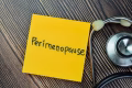 Concept of Perimenopause write on sticky notes with stethoscope isolated on Wooden Table.
