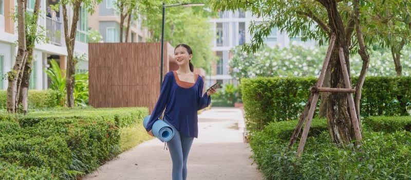 Asian Gen Z woman carrying yoga mat walking to park for wellness healthy lifestyle mindfulness and outdoor exercise